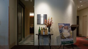 A reception area with a sign reading "ravenna," a table with bottles and a vase of flowers, and a poster on the wall. - Chisun Hotel Hamamatsucho (Tokyo)