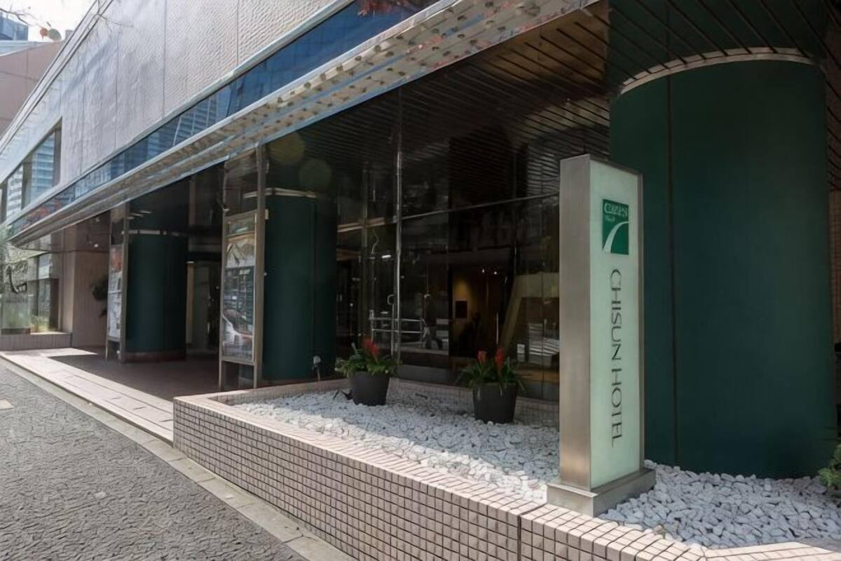 A hotel entrance with a glass facade, a signboard, and potted plants.
