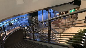 A modern interior with a curved staircase, glass railings, and a view of an outdoor area with plants. - Chisun Hotel Hamamatsucho (Tokyo)