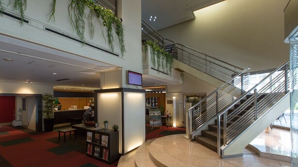 A spacious lobby with a curved staircase, a reception desk, and indoor plants. - Chisun Hotel Hamamatsucho (Tokyo)