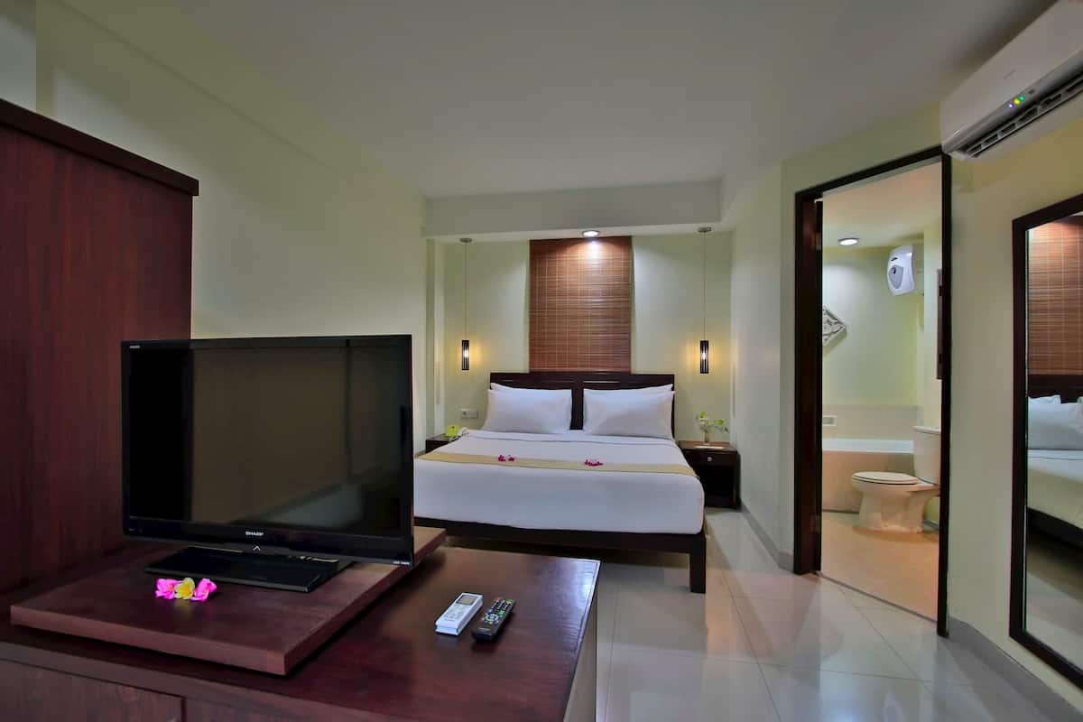 A hotel room with a bed, bedside tables, a television, and a bathroom visible through an open door.