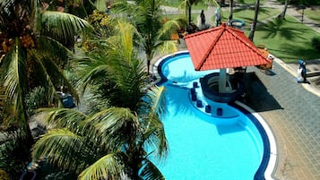 Piscina com uma estrutura de telhado vermelho, rodeada por palmeiras e um calçadão pavimentado.