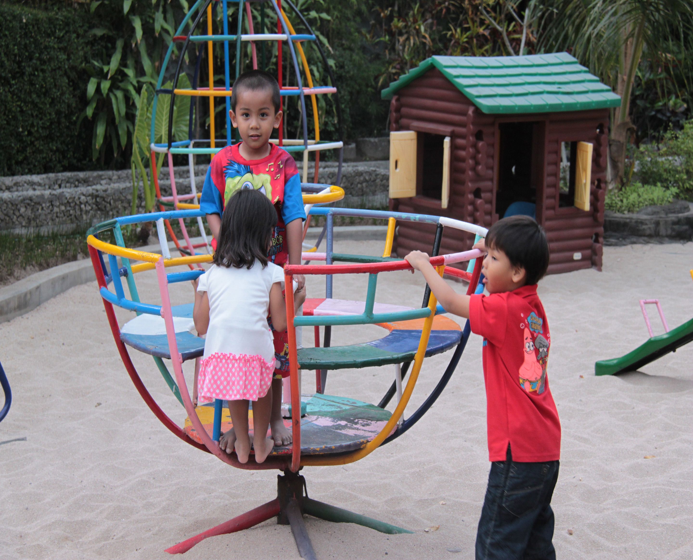 Children playing on a colorful playground structure with a log cabin in the background.