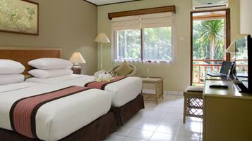 A hotel room with two beds, a desk with a laptop, a chair, a window with a view of palm trees, and a painting on the wall.