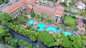 An aerial view of a resort with multiple swimming pools, lush greenery, and a large building with a red roof.