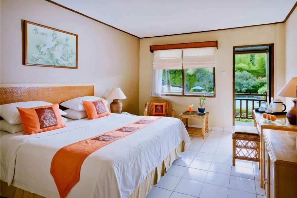 Un dormitorio con una cama grande, una mesita de noche con lámpara, una silla y una ventana con vistas a zonas verdes.