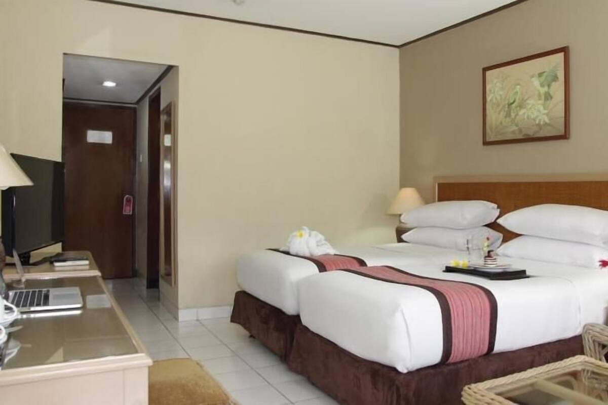 Una habitación de hotel con cama, mesitas de noche, un escritorio con ordenador y televisor.