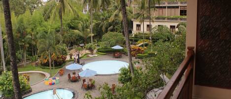A resort with multiple swimming pools surrounded by palm trees and greenery, a covered seating area, and a building with a balcony.