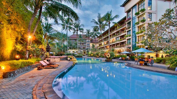 A hotel with a swimming pool, palm trees, and outdoor seating areas.