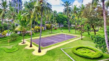 A well-maintained garden with a tennis court, palm trees, and manicured lawns.