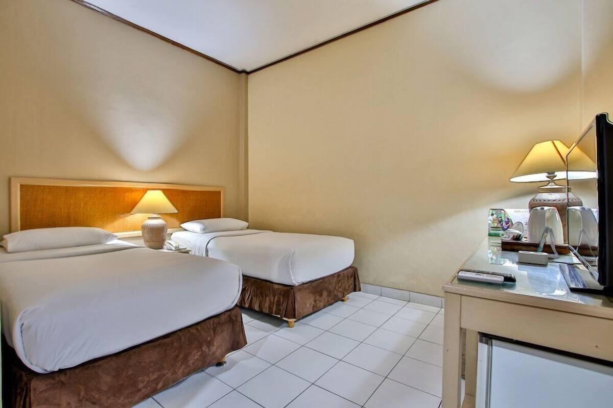 Habitación de hotel con dos camas, un escritorio con lámpara, televisión y un mini bar.