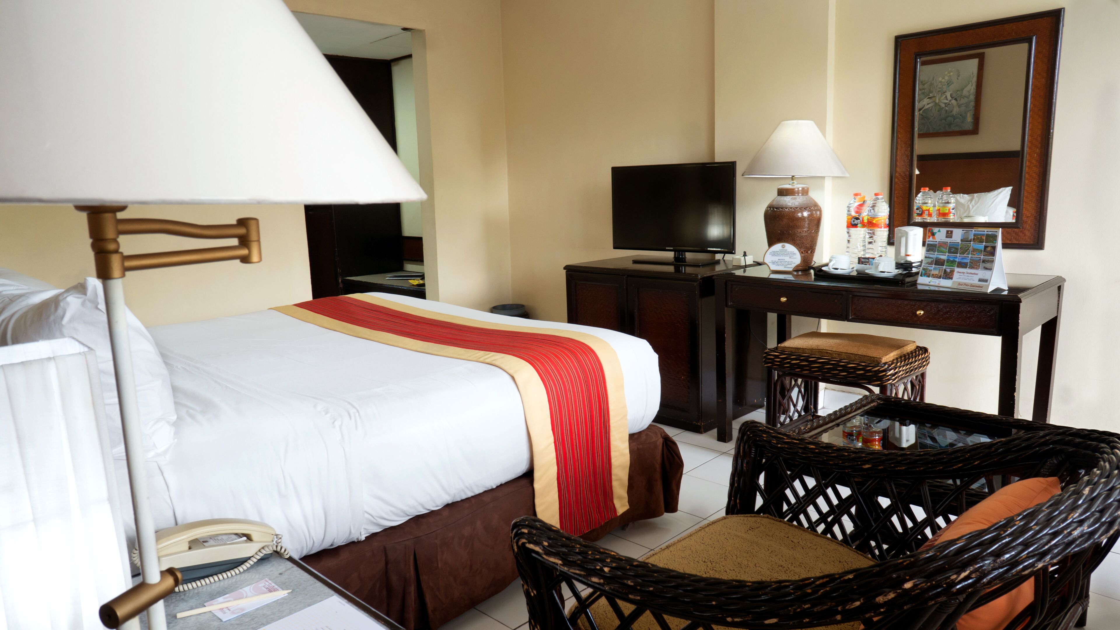 A hotel room with a bed, a desk with a television, a chair, and a lamp.