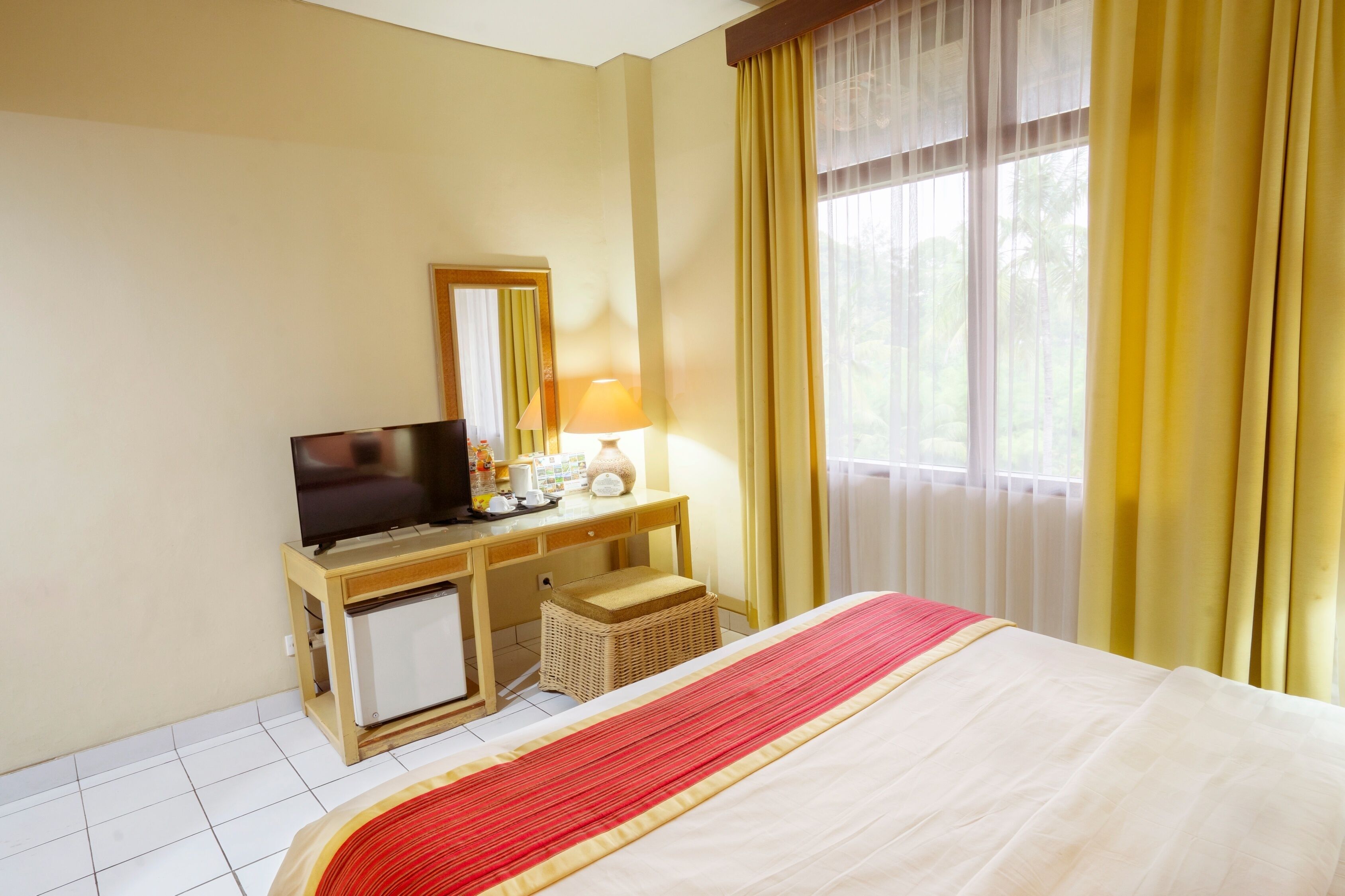 Une chambre d’hôtel avec un lit, un bureau doté d’une télévision, une lampe et une fenêtre avec des rideaux.