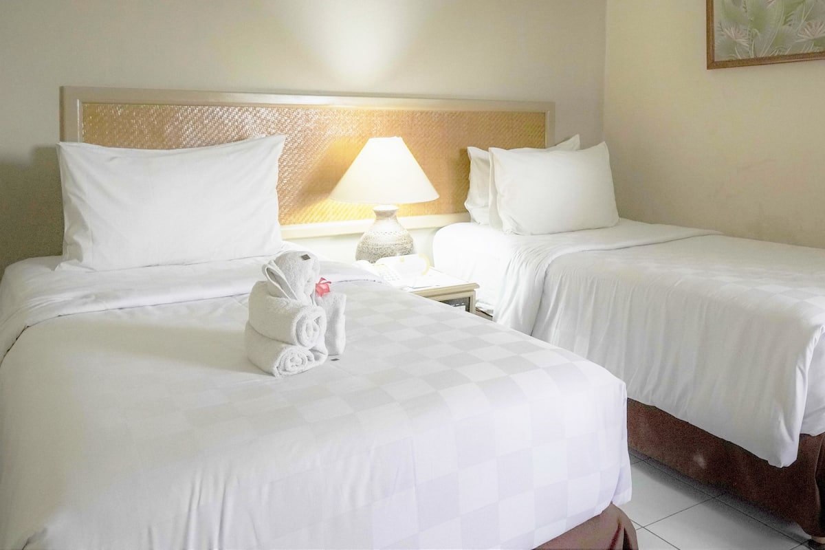 Una habitación de hotel con dos camas, una mesita de noche, una lámpara y un cuadro en la pared.