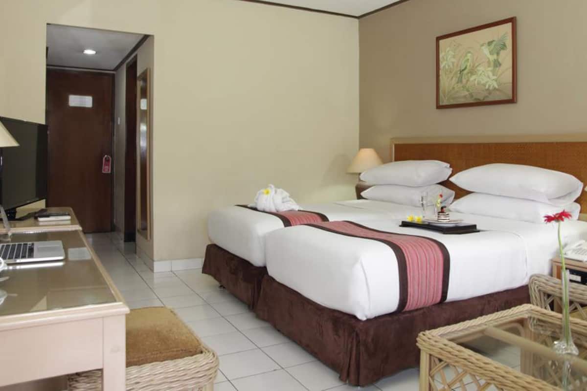 Una habitación de hotel con cama, mesitas de noche, un escritorio, televisión y un cuadro en la pared.