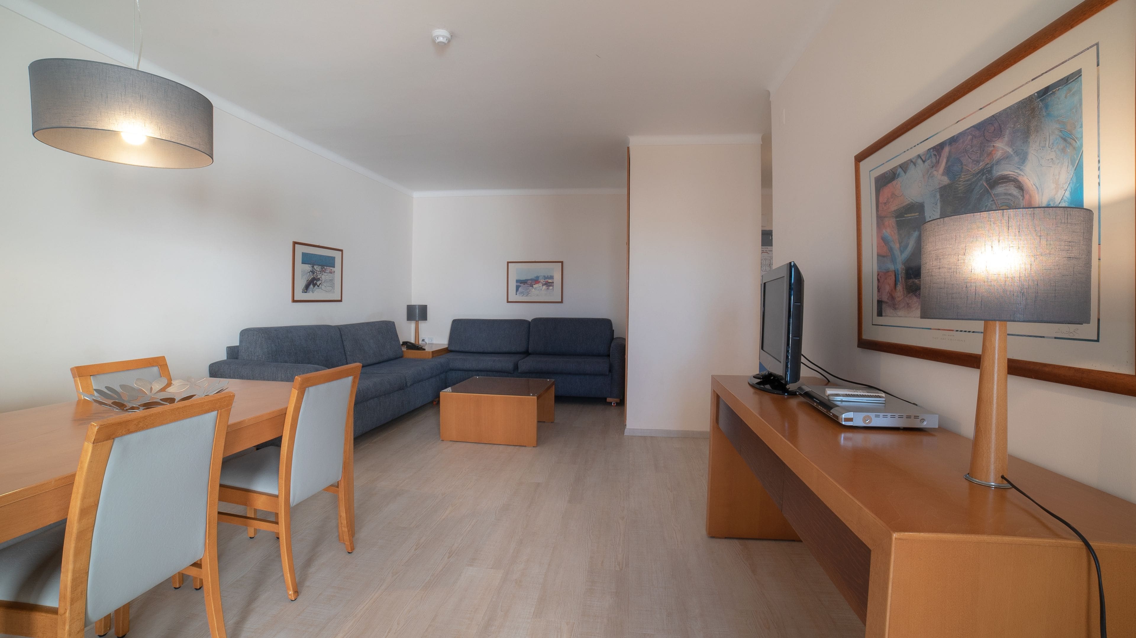 Un salon moderne comprenant un canapé, une table à manger avec des chaises, un téléviseur et une lampe.