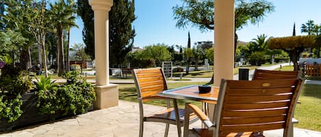 A covered outdoor seating area with stone flooring, wooden chairs, and a table.