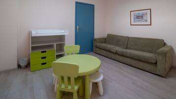 Una habitación con una mesa y sillas verdes, un sofá color beige, una puerta azul y un cuadro en la pared.