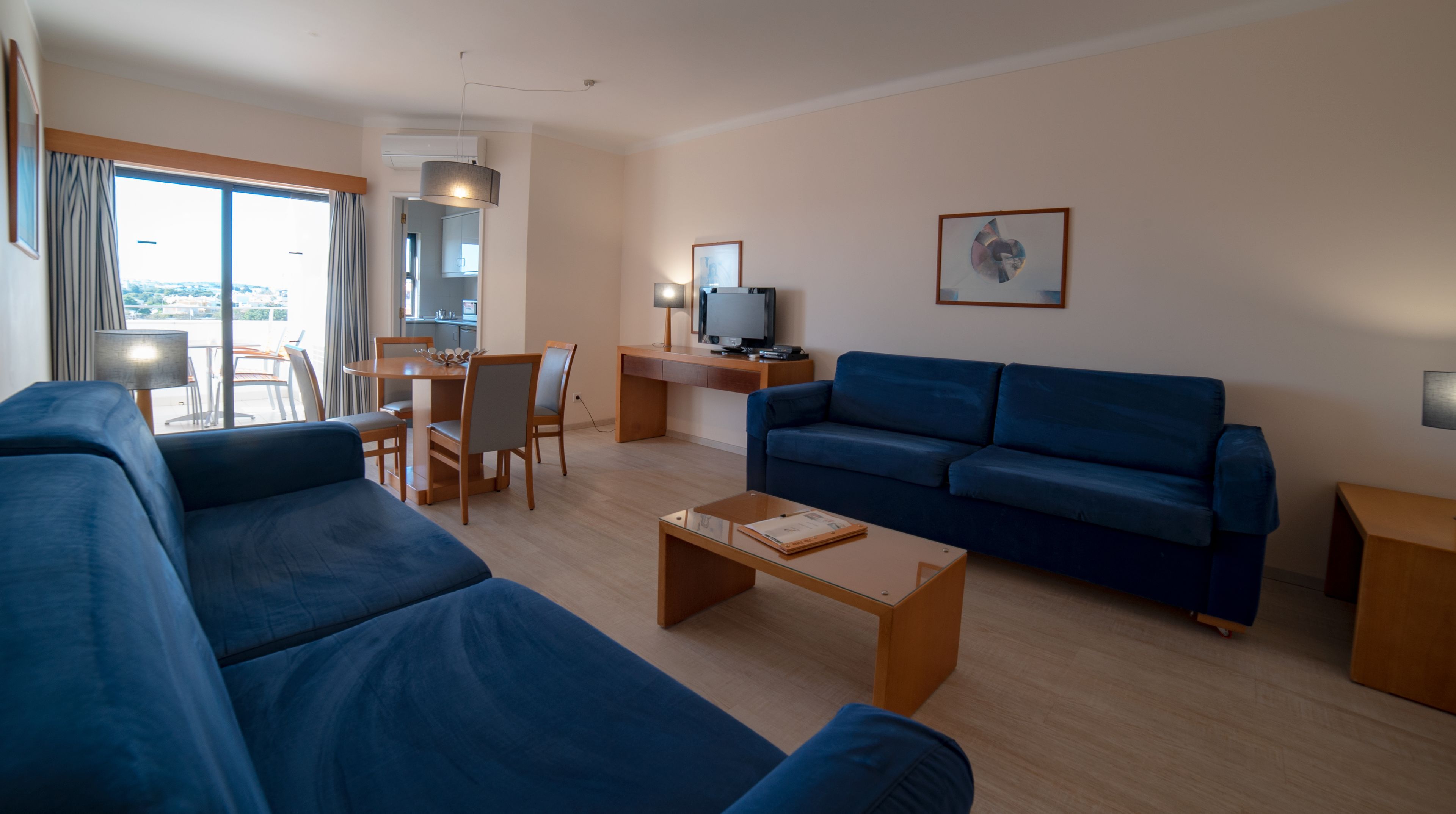 Una sala de estar moderna con un sofá azul, una mesa de centro de madera y un área de comedor con una mesa y sillas.