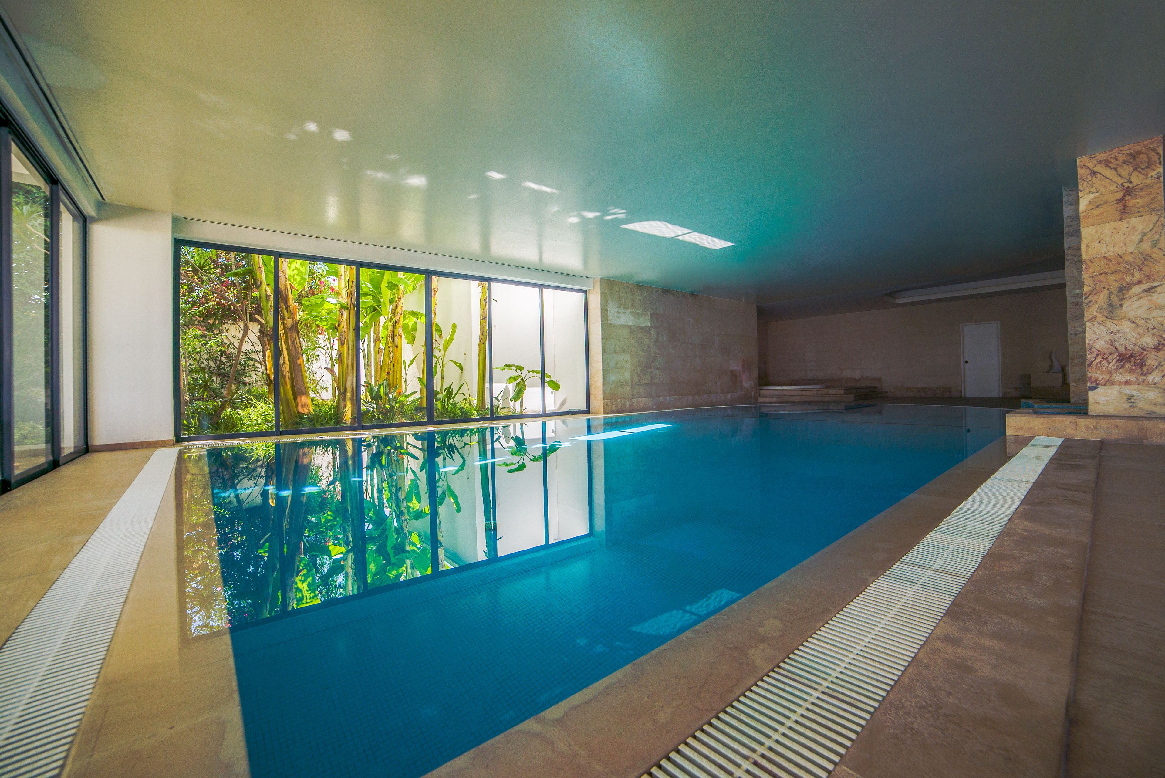 An indoor swimming pool with clear glass walls, a tiled floor, and a view of greenery outside.