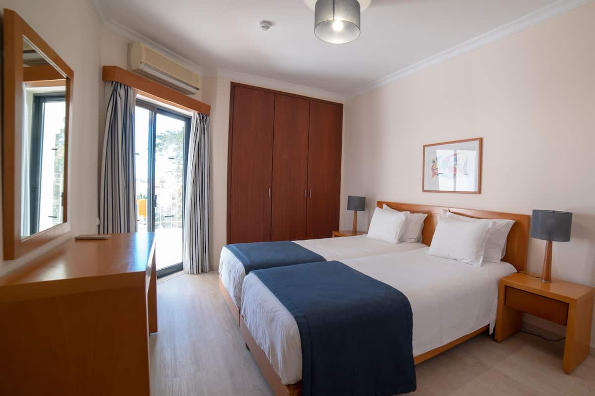 A hotel room with a large bed, two bedside tables, a wardrobe, and a window with curtains.