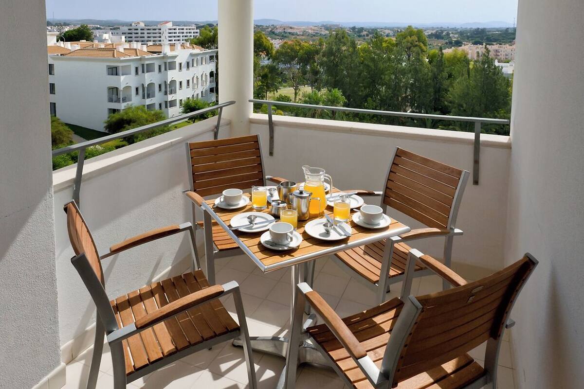 A balcony with a table set for breakfast, including plates, cups, and orange juice.