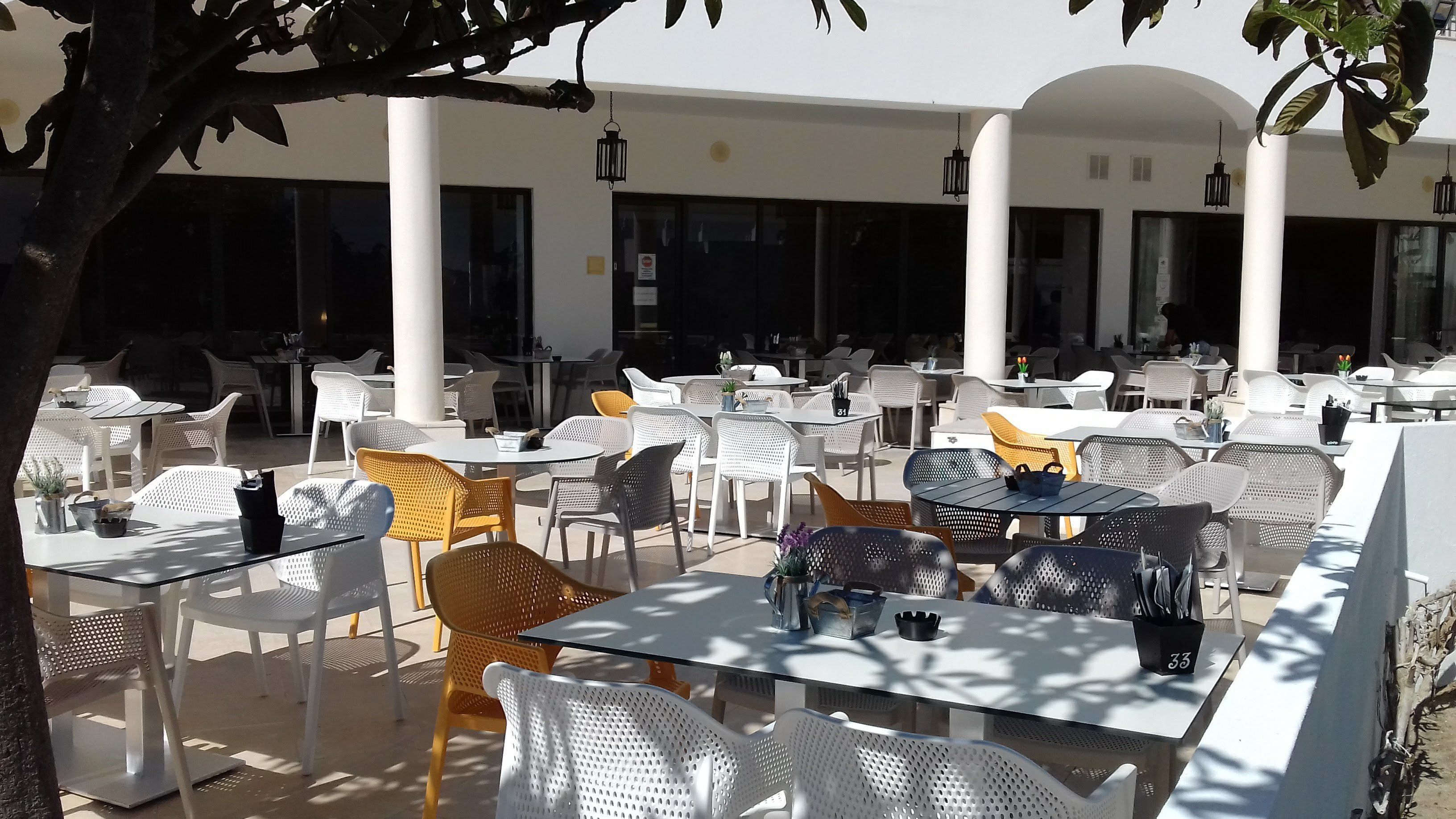 Ein Straßencafé mit weißen und gelben Stühlen, Tischen und hängenden Laternen.