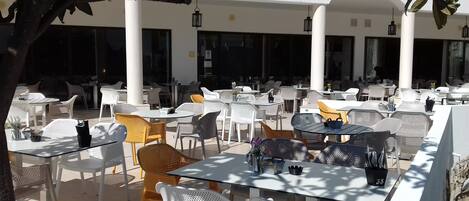 Ein Straßencafé mit weißen und gelben Stühlen, Tischen und hängenden Laternen.