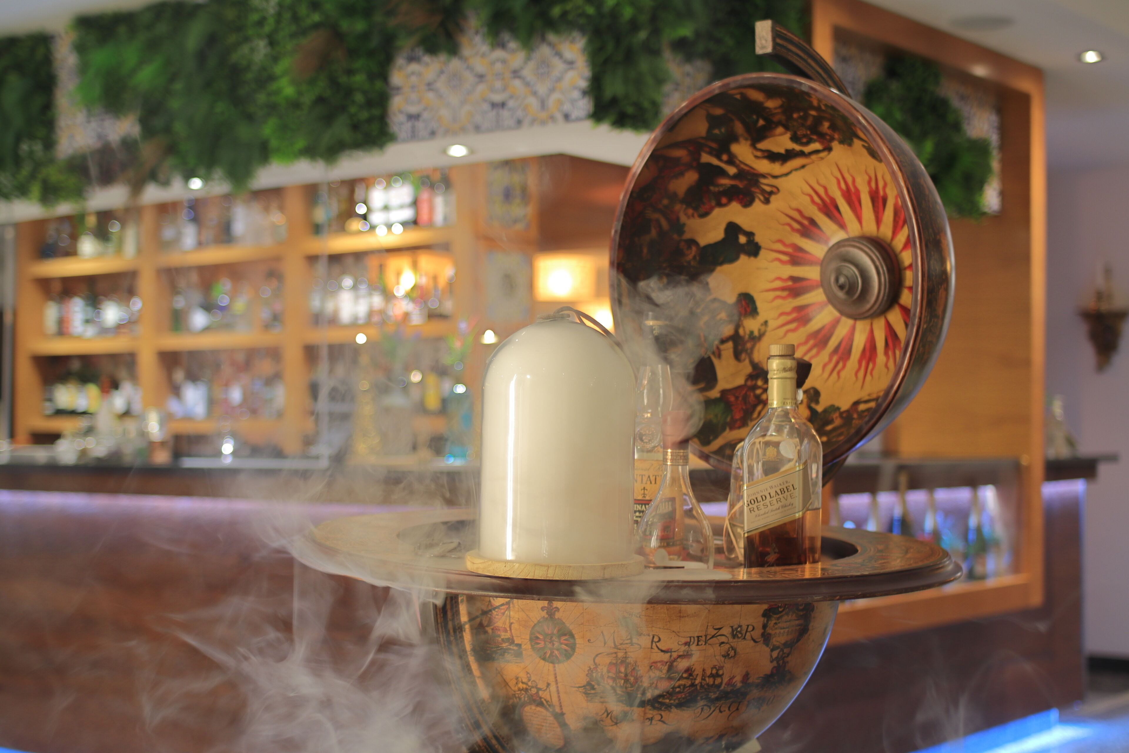 Een bar met een decoratieve glazen schaal waarin een fles en een wit object zitten dat stoom uitstoot.