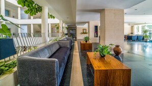 A modern lobby with a grey sofa, wooden tables, and potted plants.