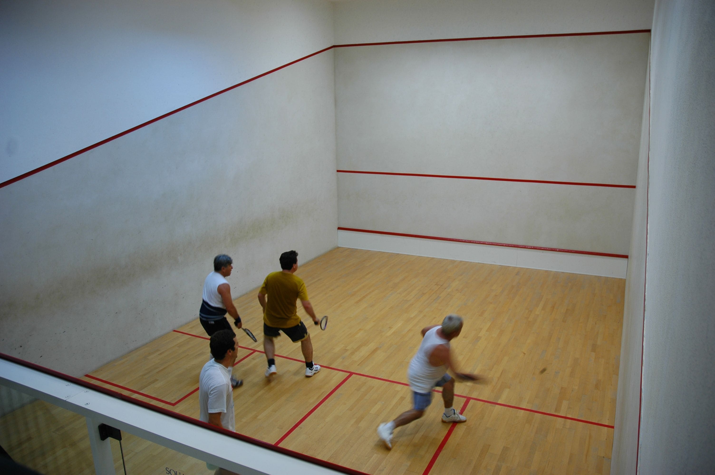 A squash court with wooden flooring and red boundary lines.