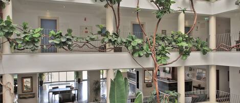 A multi-level atrium with indoor plants, a reception desk, and seating areas.