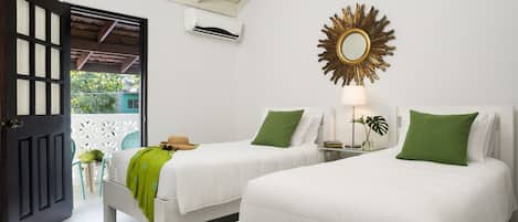 A hotel room with two beds, a ceiling fan, an air conditioning unit, a decorative mirror, and a view of the outside.