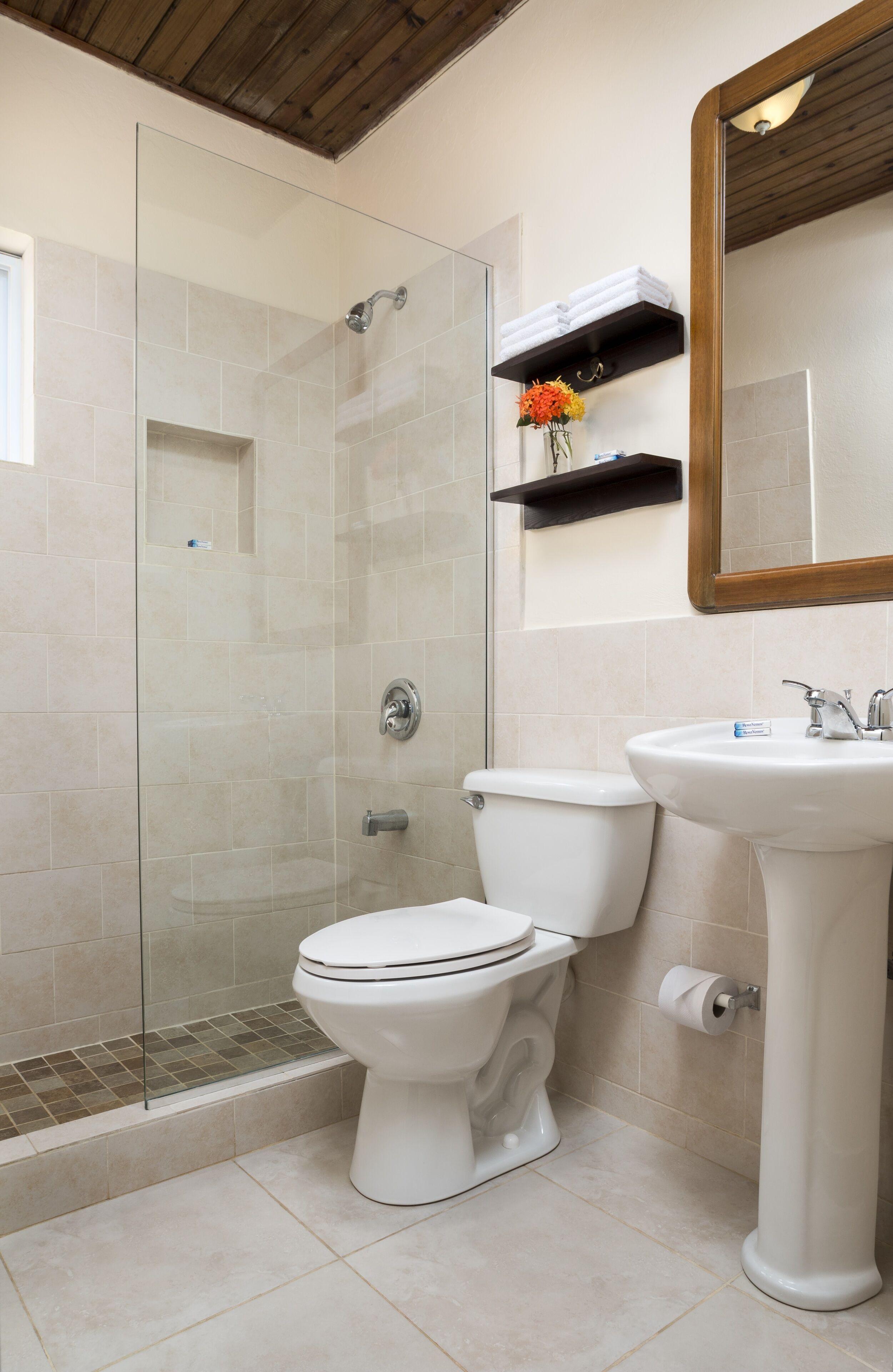A bathroom with a glass-enclosed shower, a toilet, a sink, and a mirror.
