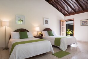 Habitación de hotel con dos camas, una mesita de noche con lámpara, una planta en maceta y obras de arte en las paredes.