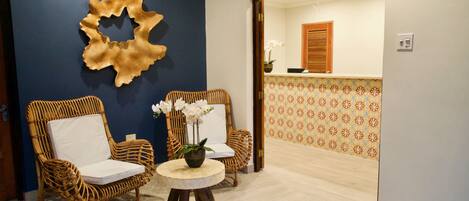 A reception area with two wicker chairs, a small round table with a plant, and a decorative wall piece.
