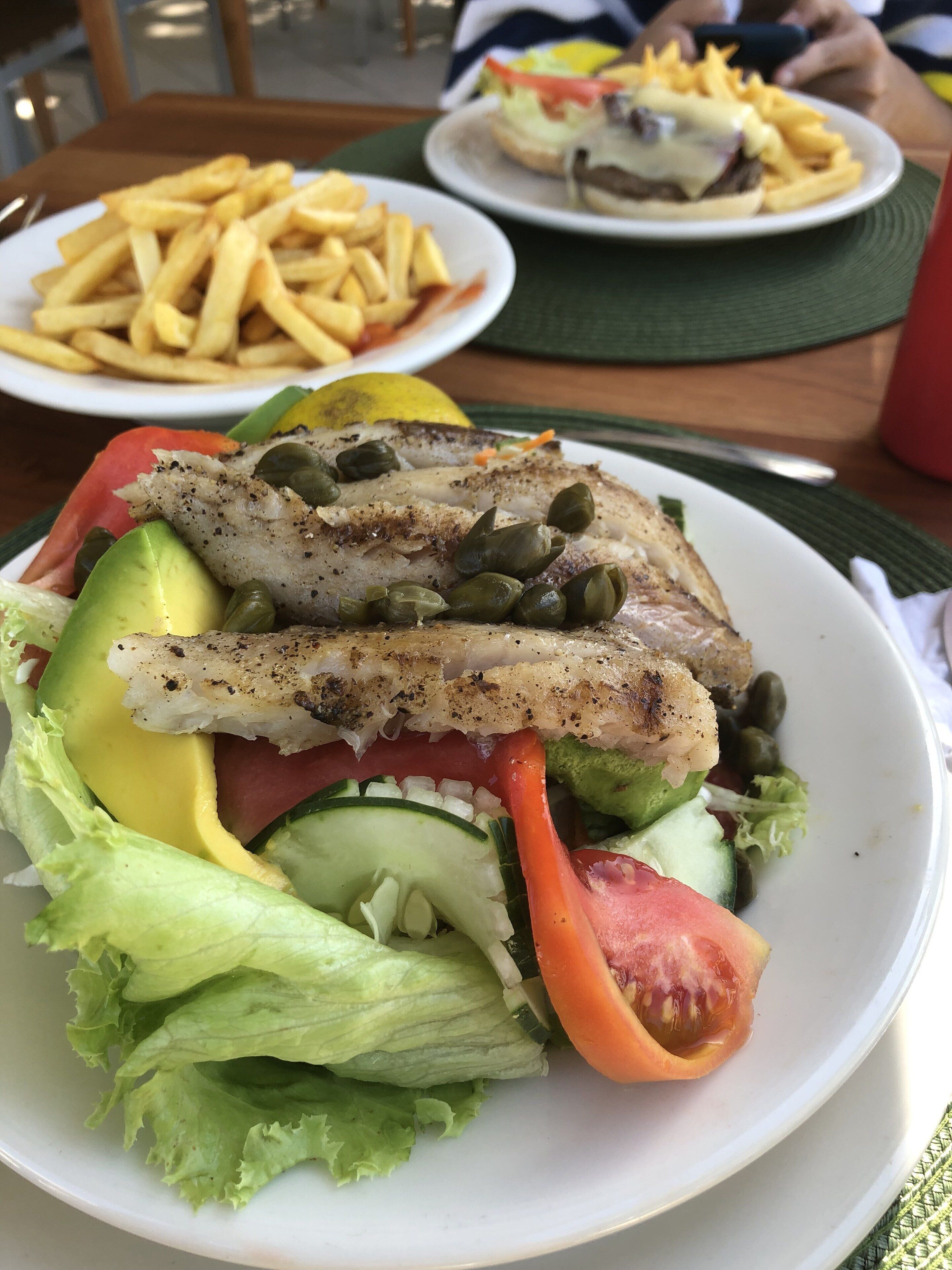 Un plato de comida con filete de pescado, aguacate, pepino, tomate y lechuga.