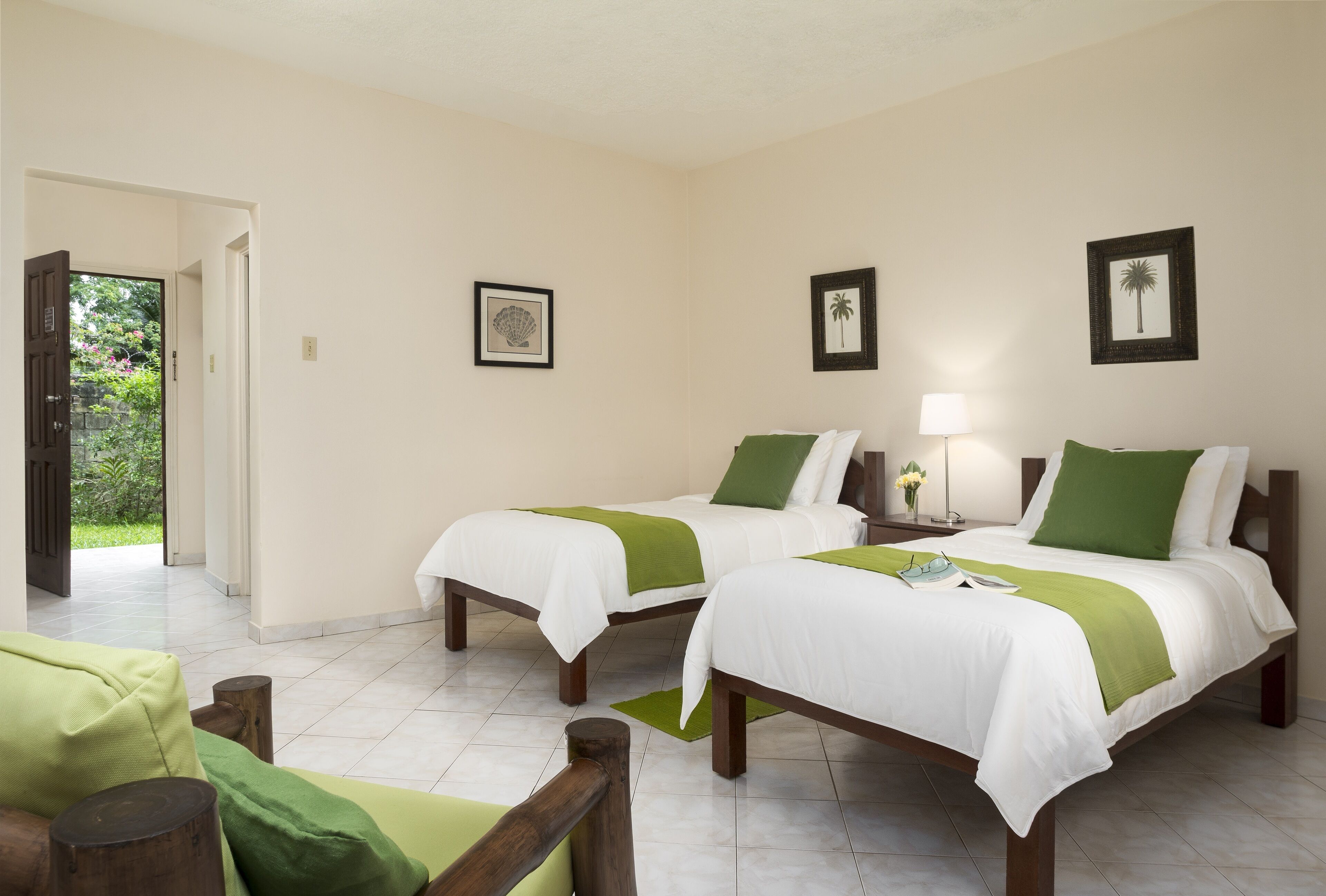 Een hotelkamer met twee bedden, een houten stoel en een deur naar een tuin.
