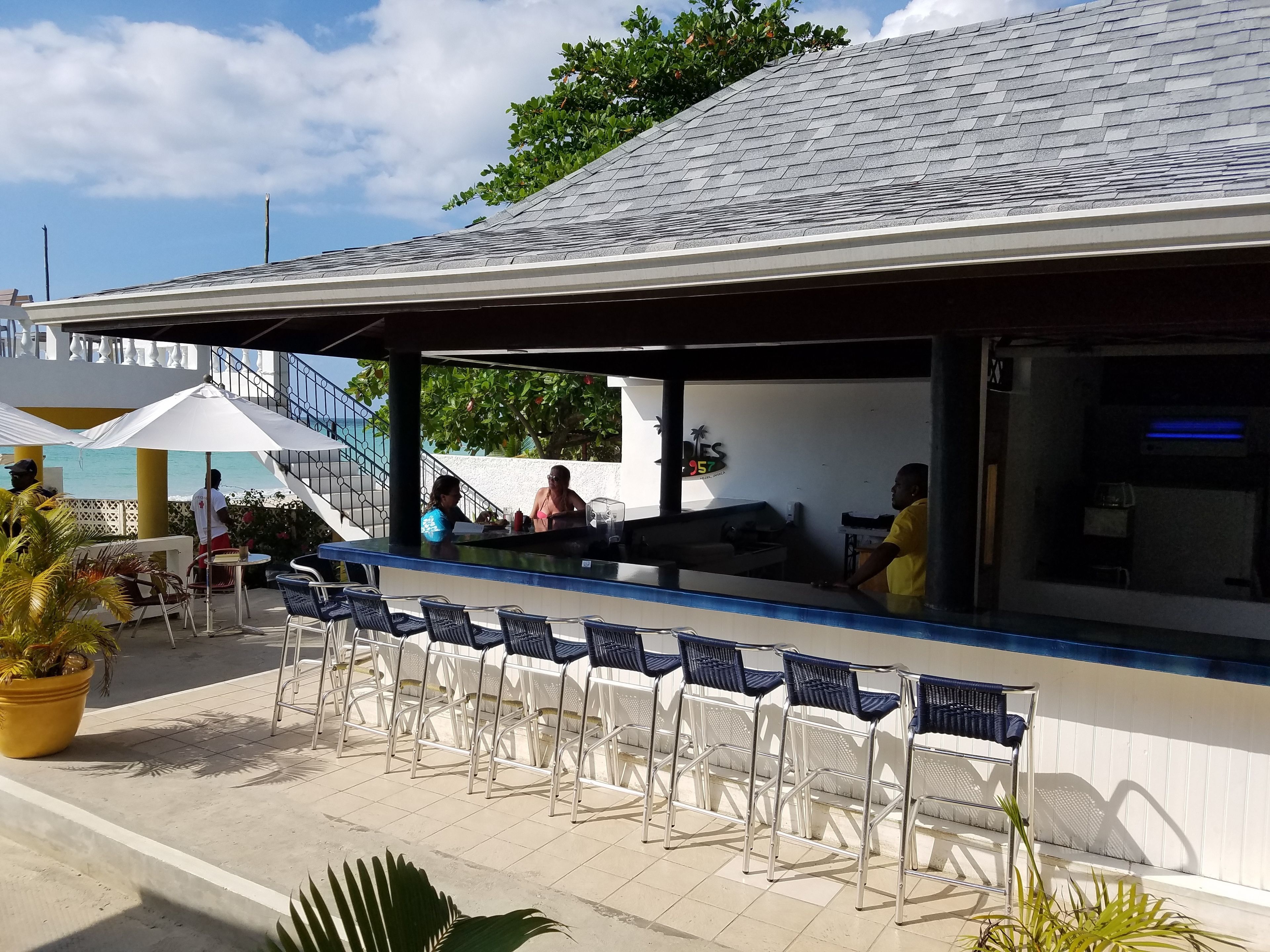 An outdoor bar area with a counter, chairs, and a view of the sea.