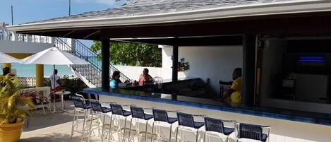 An outdoor bar area with a counter, chairs, and a view of the sea.