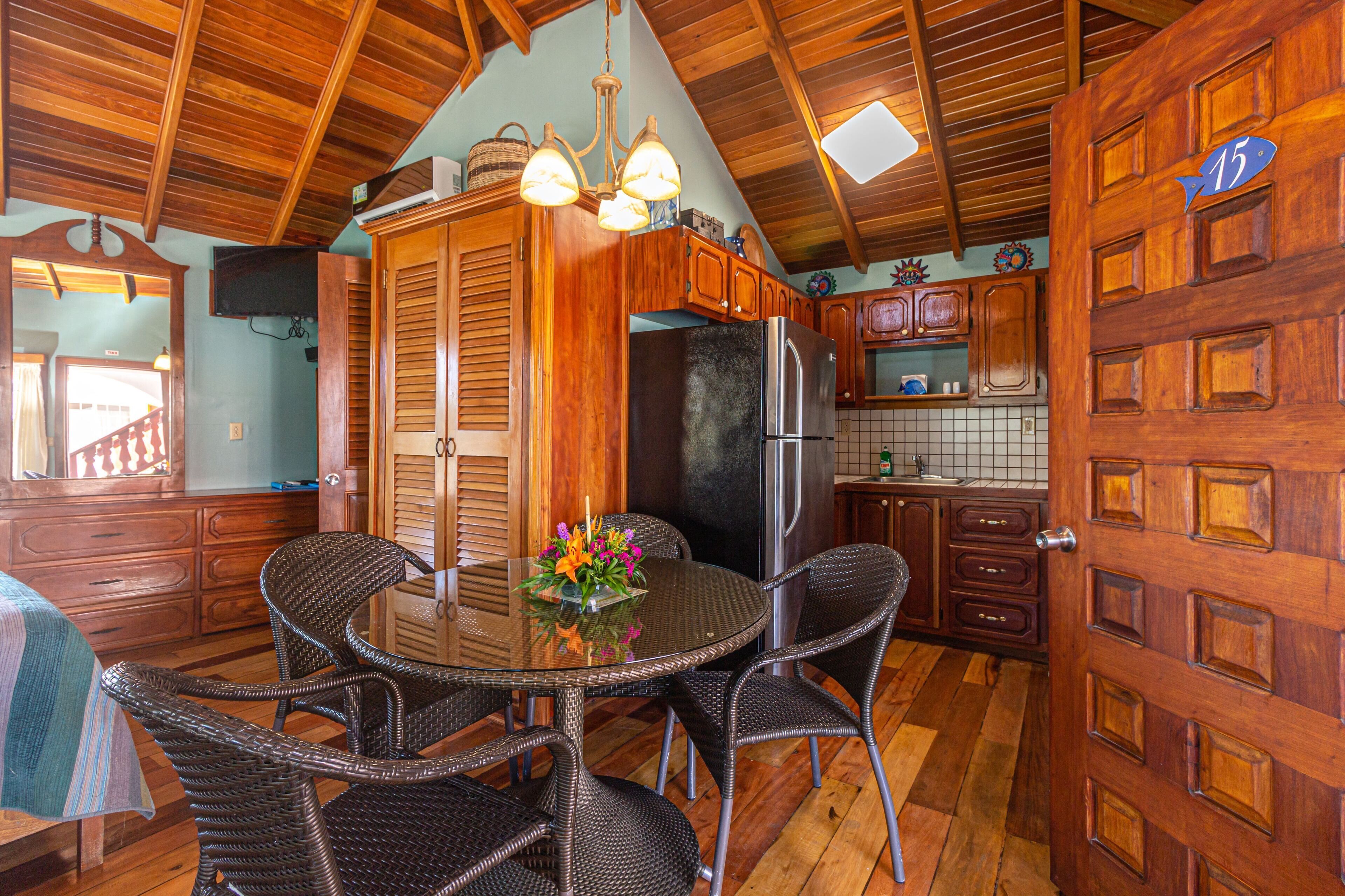 Una cocina de madera con una mesa de comedor, sillas de mimbre, un refrigerador y una puerta de madera con el número 15.