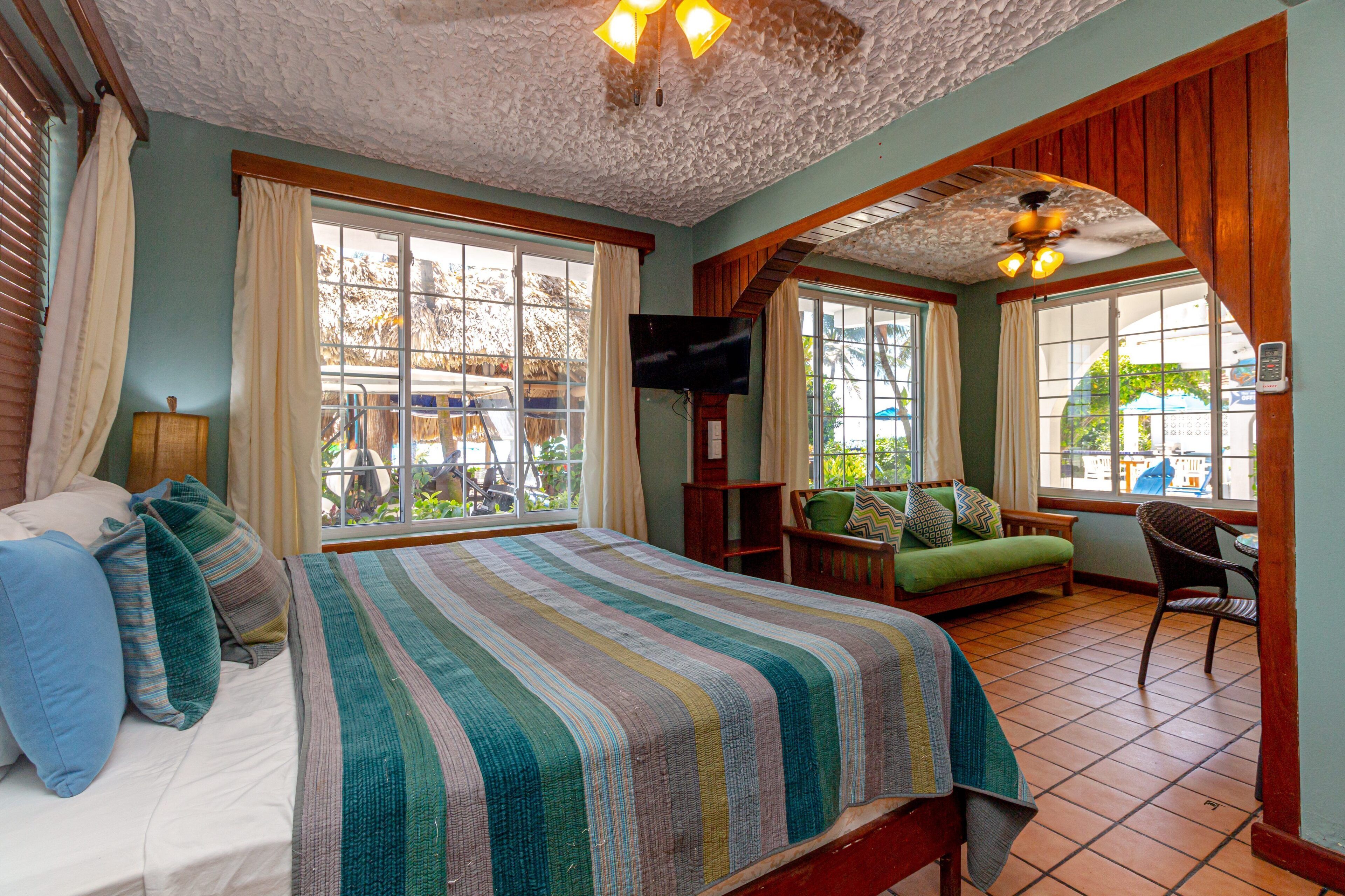 A bedroom with a bed, a TV, a sofa, and a chair.
