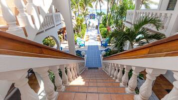 A staircase with white balustrades leading to a pool area with blue chairs and palm trees.