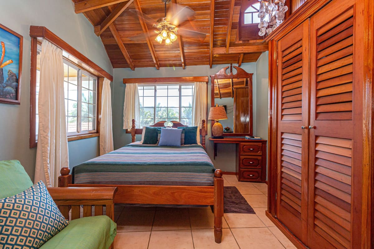 A bedroom with a wooden bed, a desk, a wardrobe, and a ceiling fan.