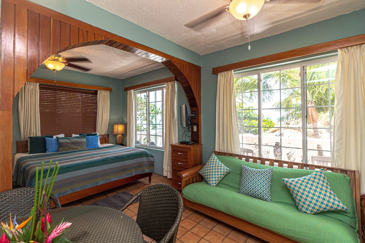A room with a bed, a green sofa, a dining table, and a ceiling fan.