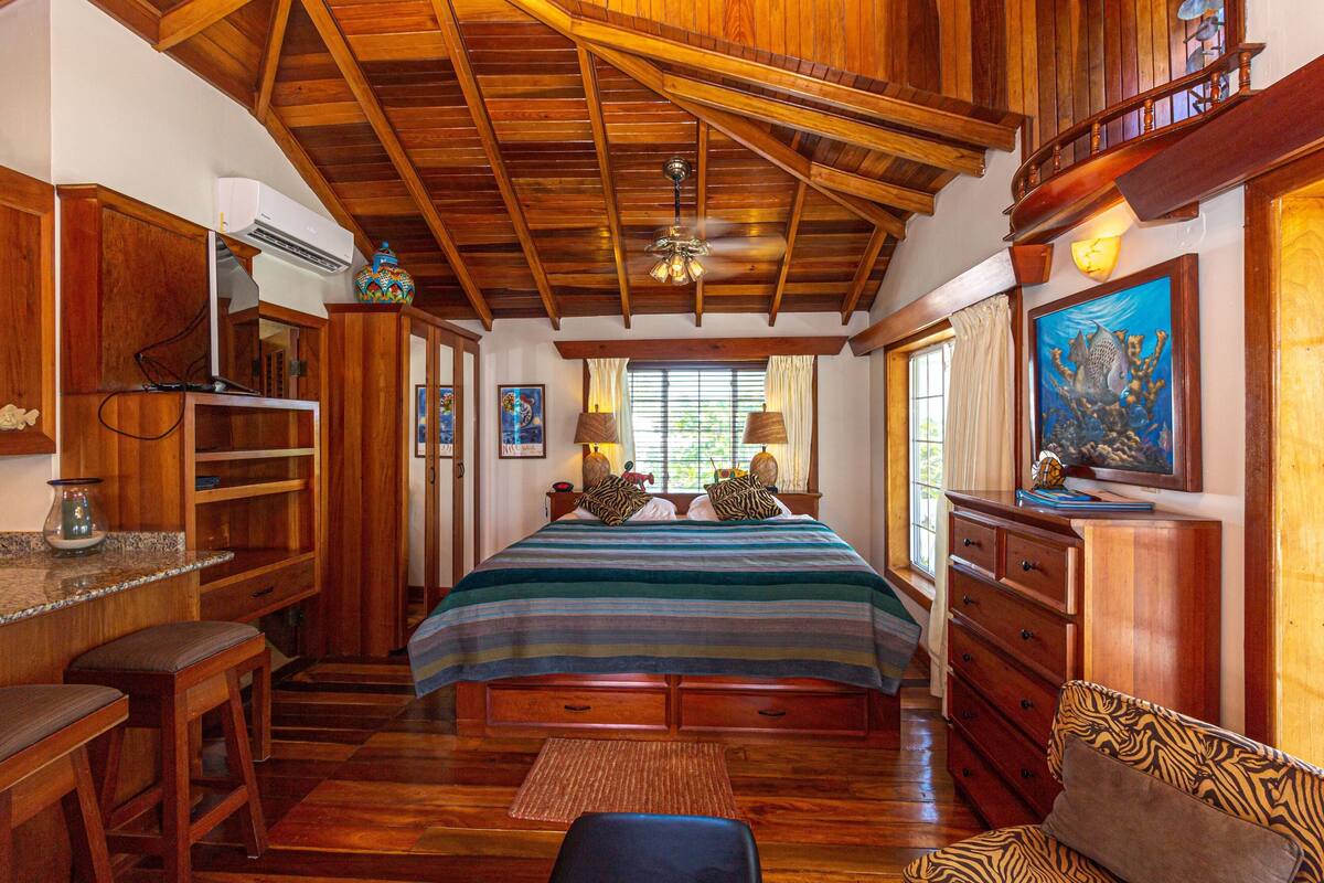 A spacious bedroom with a large bed, wooden ceiling beams, a built-in desk, and a cozy seating area.