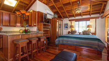 A wooden interior with a kitchen area, bar stools, a bed with a striped bedspread, and a ceiling fan.