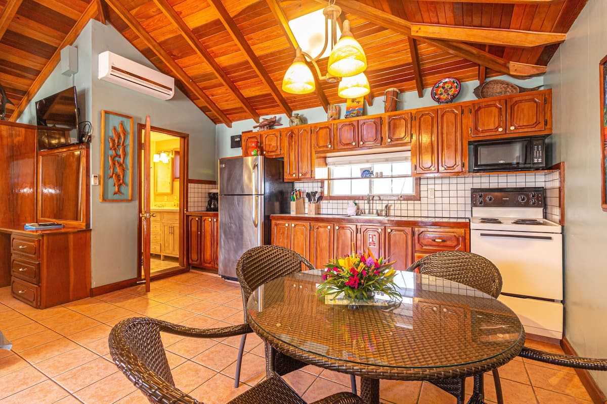 A kitchen with wooden cabinets, a refrigerator, a microwave, and a stove. There is a dining table with chairs and a vase of flowers.