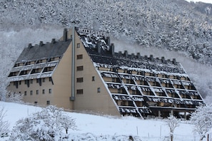 A hotel with a sloped roof and multiple windows, surrounded by snow-covered trees and hills. -  RVHotels Tuca (Vielha e Mijaran)