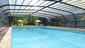 A covered swimming pool with a glass roof, two white lounge chairs, and a wooden deck area. -  RVHotels Tuca (Vielha e Mijaran)